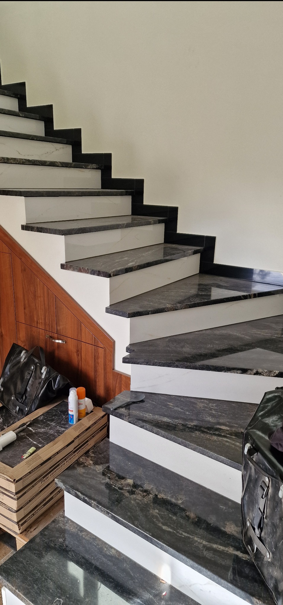 Schody z czarnego granitu z białymi podstopnicami, częściowo wykończone, widoczne materiały budowlane i narzędzia pracy, realizacja we Wrocławiu.
