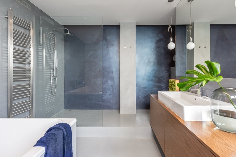 Nowoczesna łazienka z kabiną prysznicową typu walk-in, grzejnikiem drabinkowym, umywalką nablatową na drewnianej szafce i dekoracyjną ścianą w odcieniach granatu i szarości.
