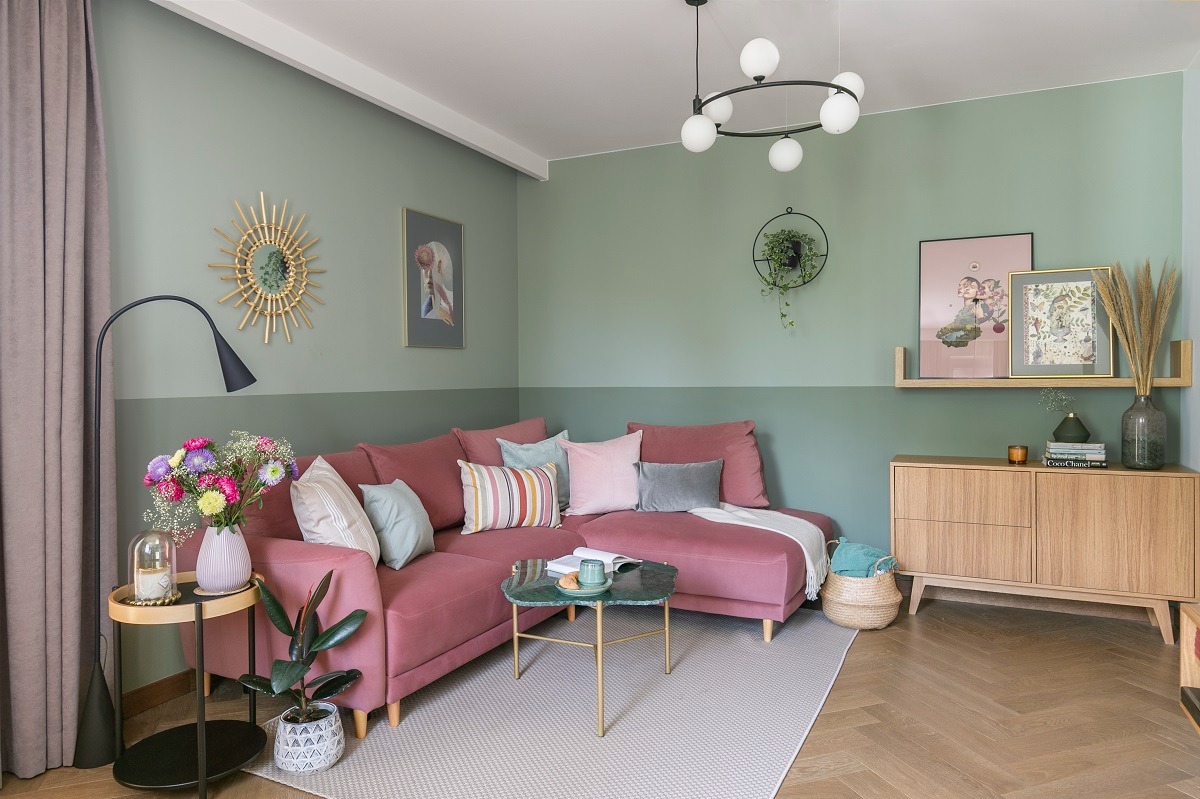 Kraków, mieszkanie 43m2: Salon z narożną sofą w odcieniach różu, zielone ściany z poziomym podziałem kolorystycznym, okrągły stolik kawowy z marmurowym blatem, drewniana komoda z dekoracjami...
