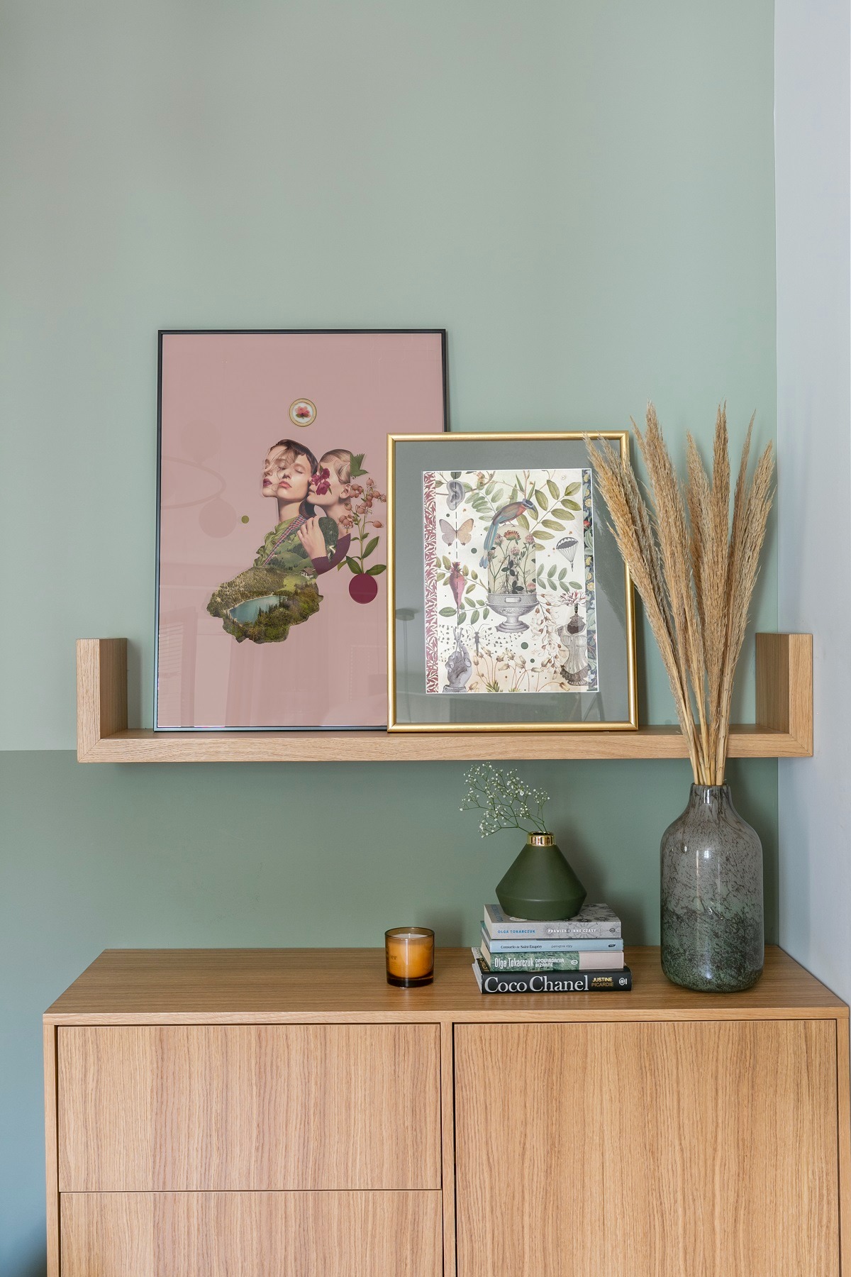 Ustawienie na drewnianej komodzie: świeca zapachowa, stos książek z tytułem 'Coco Chanel', mały wazon z gipsówką, wysoki wazon z suszonymi trawami, grafiki w ramkach na półce, ściana w dwóch...