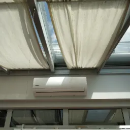 Klimatyzator Kaisai zamontowany pod przeszklonym dachem z beżowymi, materiałowymi roletami, widok od dołu.