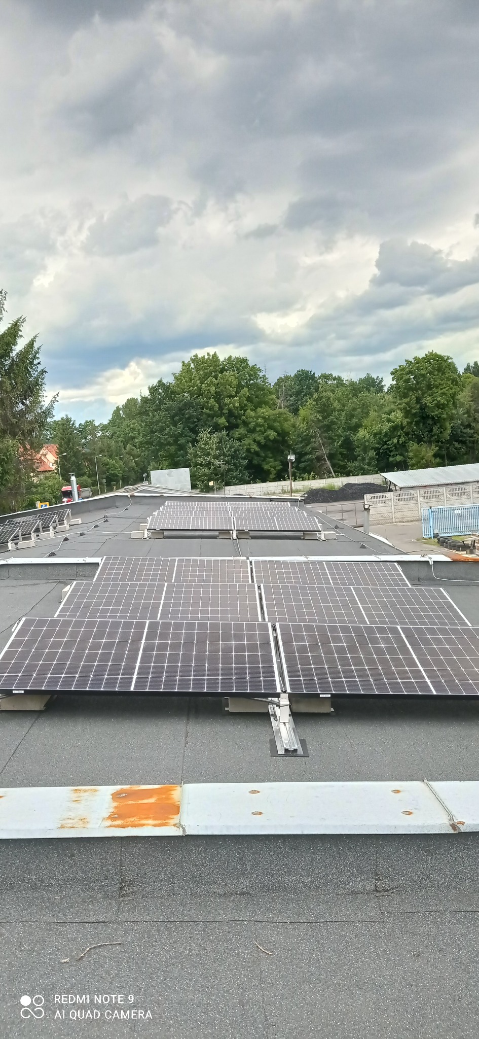 Panele słoneczne zamontowane na płaskim dachu budynku, widok z góry w pochmurny dzień.