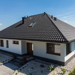 Dom jednorodzinny z ciemną dachówką karpiówką, widok z góry na elewację i uporządkowany teren wokół budynku.