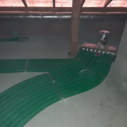 Rozprowadzenie zielonych rur rekuperacji na poddaszu, widoczny rozdzielacz i ocieplone przewody wentylacyjne pod dachem.