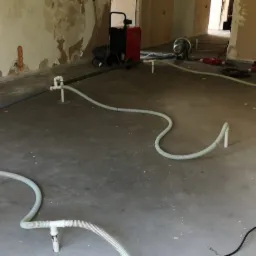 Sprzęt do usuwania wilgoci z posadzki w pomieszczeniu w trakcie remontu, widoczne rury wentylacyjne i urządzenie osuszające.