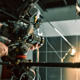 INNOVA SYSTEM Robert Przybyłek - Profesjonalna kamera filmowa na statywie, z widocznymi rękami operatora, oświetlenie studyjne w tle, ujęcie z bliska.