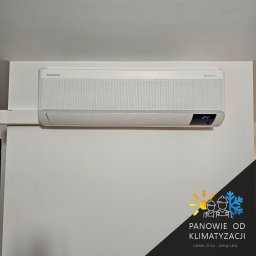 Panowie od Klimatyzacji - Klimatyzacja, Pompy Ciepła, Chłodnictwo. - Biała klimatyzacja Samsung WindFree zamontowana na ścianie w Czarna Woda. Widoczny wyświetlacz z temperaturą 24 stopnie. Minimalistyczny design i biała maskownica kabli.