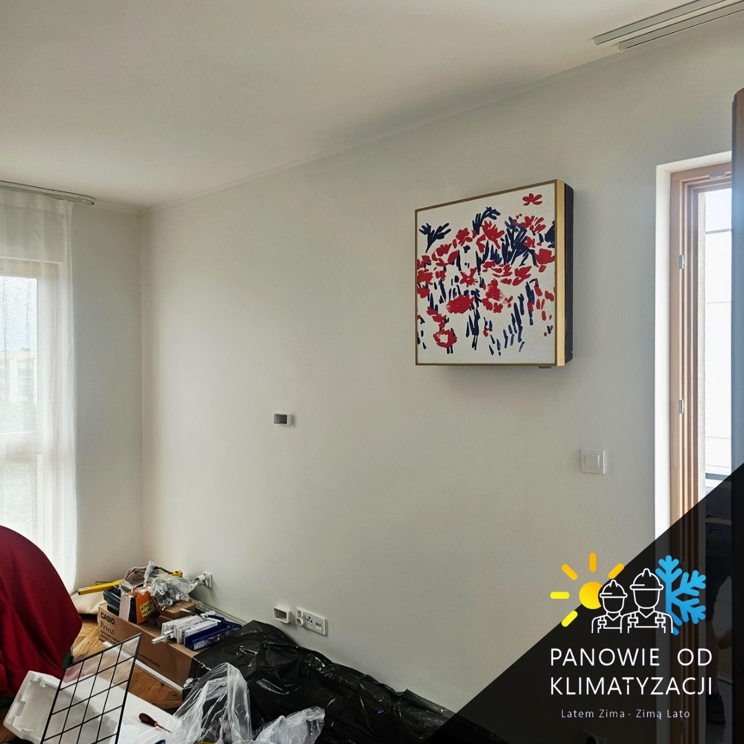 Wnętrze pokoju z zamontowaną klimatyzacją kasetonową pod sufitem. Na ścianie wisi obraz. Widoczne narzędzia i materiały instalacyjne.