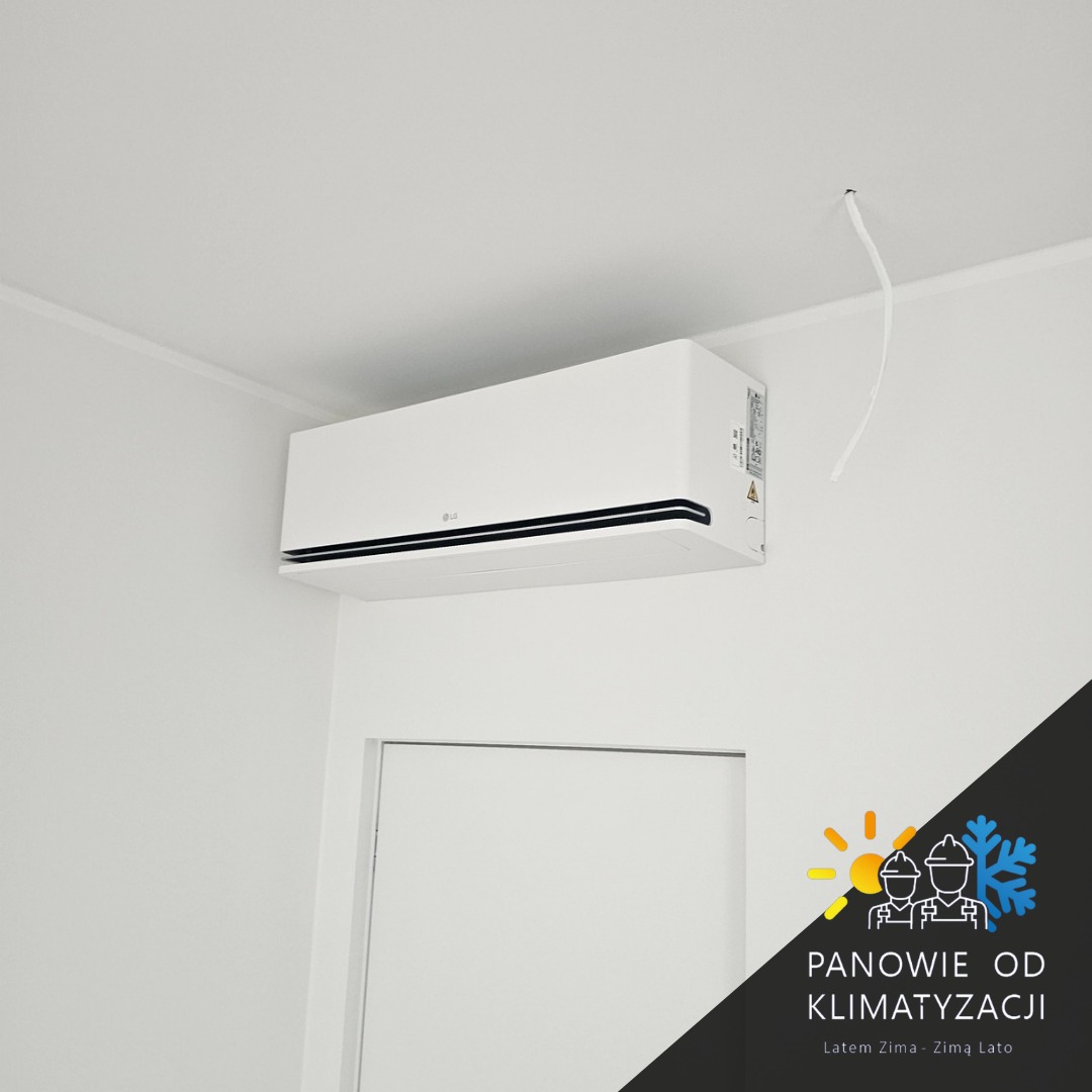 Biała klimatyzacja LG zamontowana na ścianie w jasnym wnętrzu, widoczne kable wystające z sufitu. Minimalistyczny design, nowoczesne wykończenie.