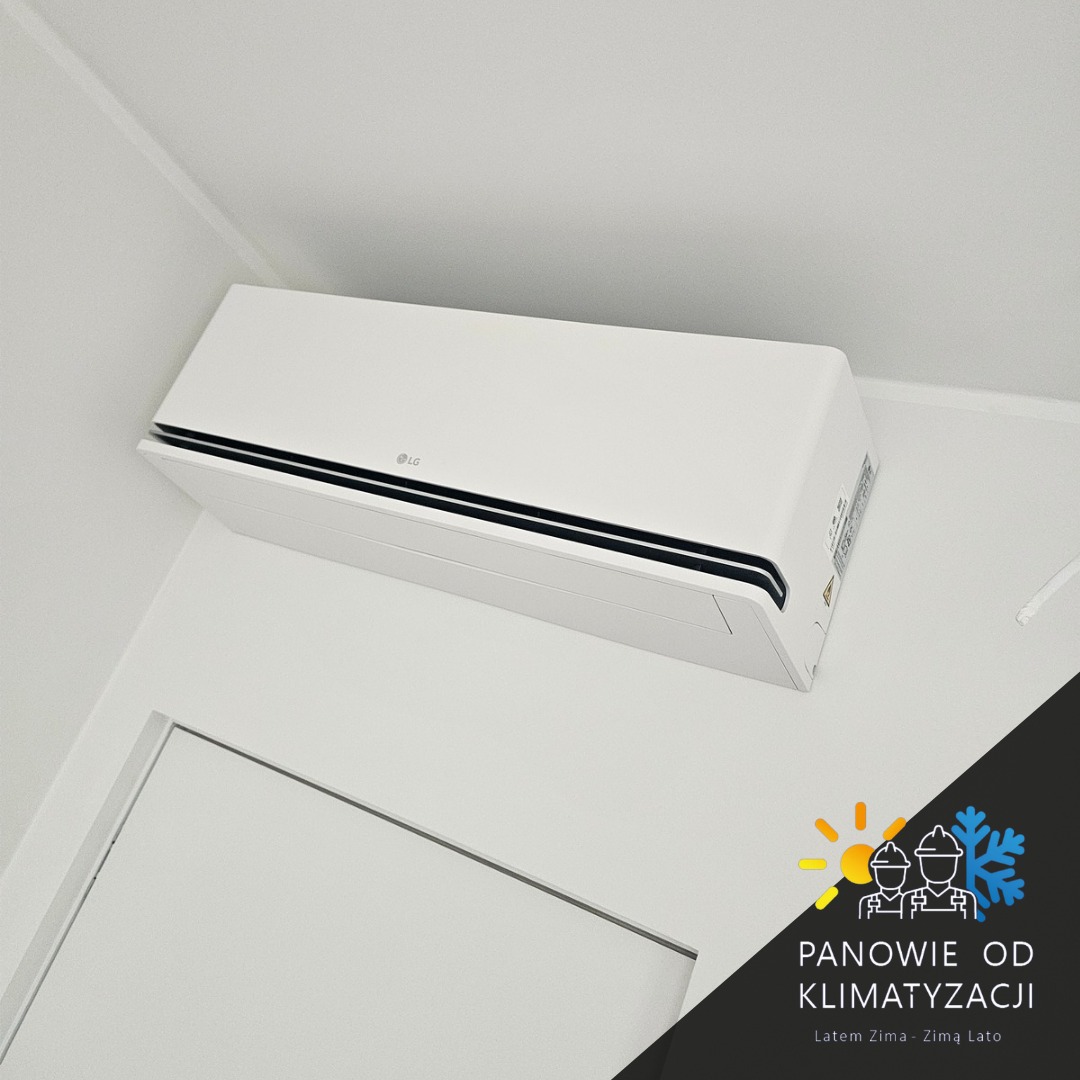Biała klimatyzacja LG zamontowana na ścianie w jasnym pomieszczeniu. Widoczny fragment drzwi i logo firmy instalacyjnej w rogu. Minimalistyczny design.