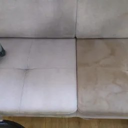 Czyszczenie jasnobeżowej kanapy z widocznymi plamami, na jednej połowie już wyczyszczonej, z użyciem odkurzacza piorącego Karcher z żółtymi elementami.