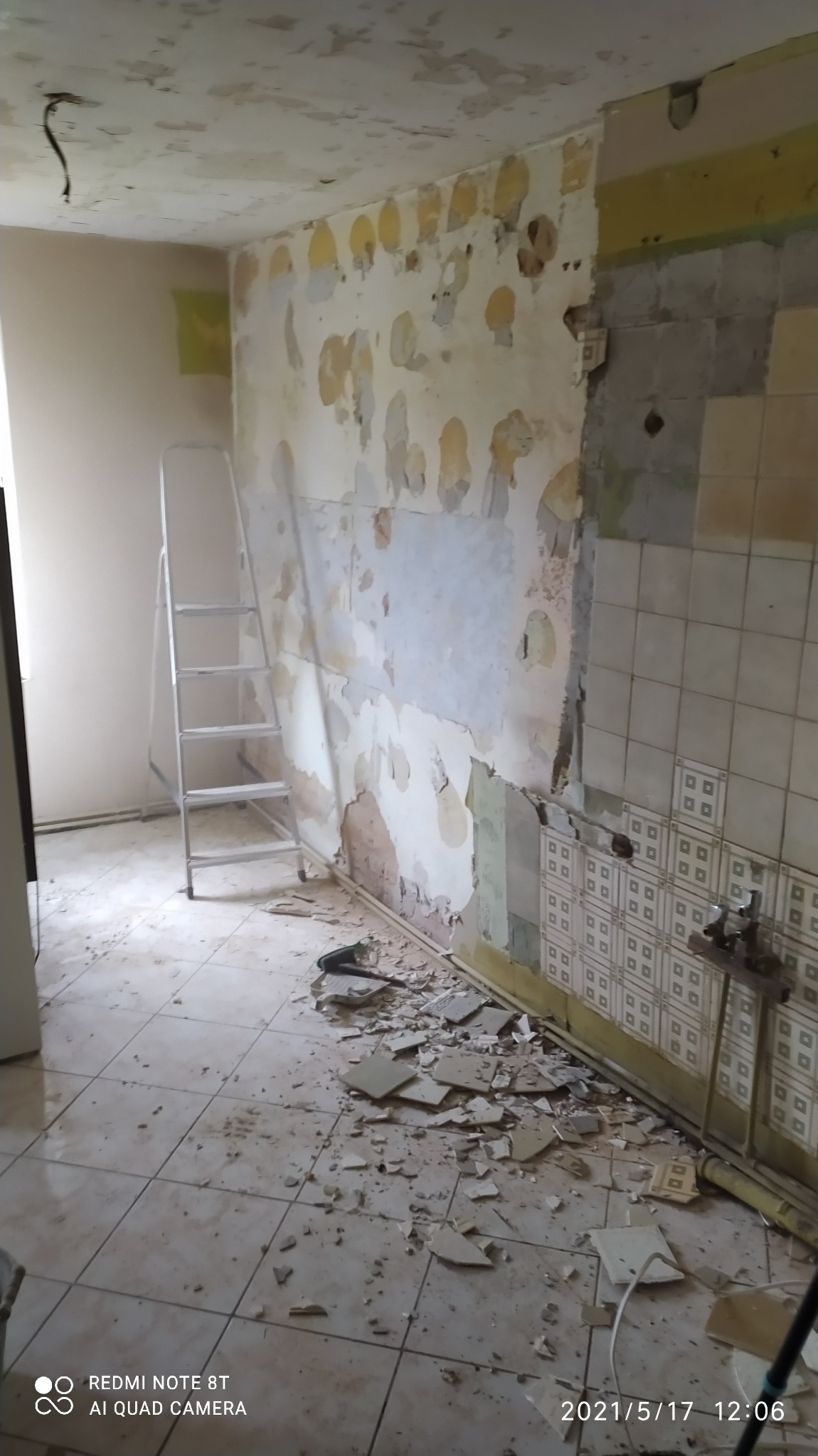 Kuchenne wnętrze w trakcie demontażu starych płytek i przygotowania ścian do remontu; widoczne resztki kleju, odspojone fragmenty tynku i drabina aluminiowa.
