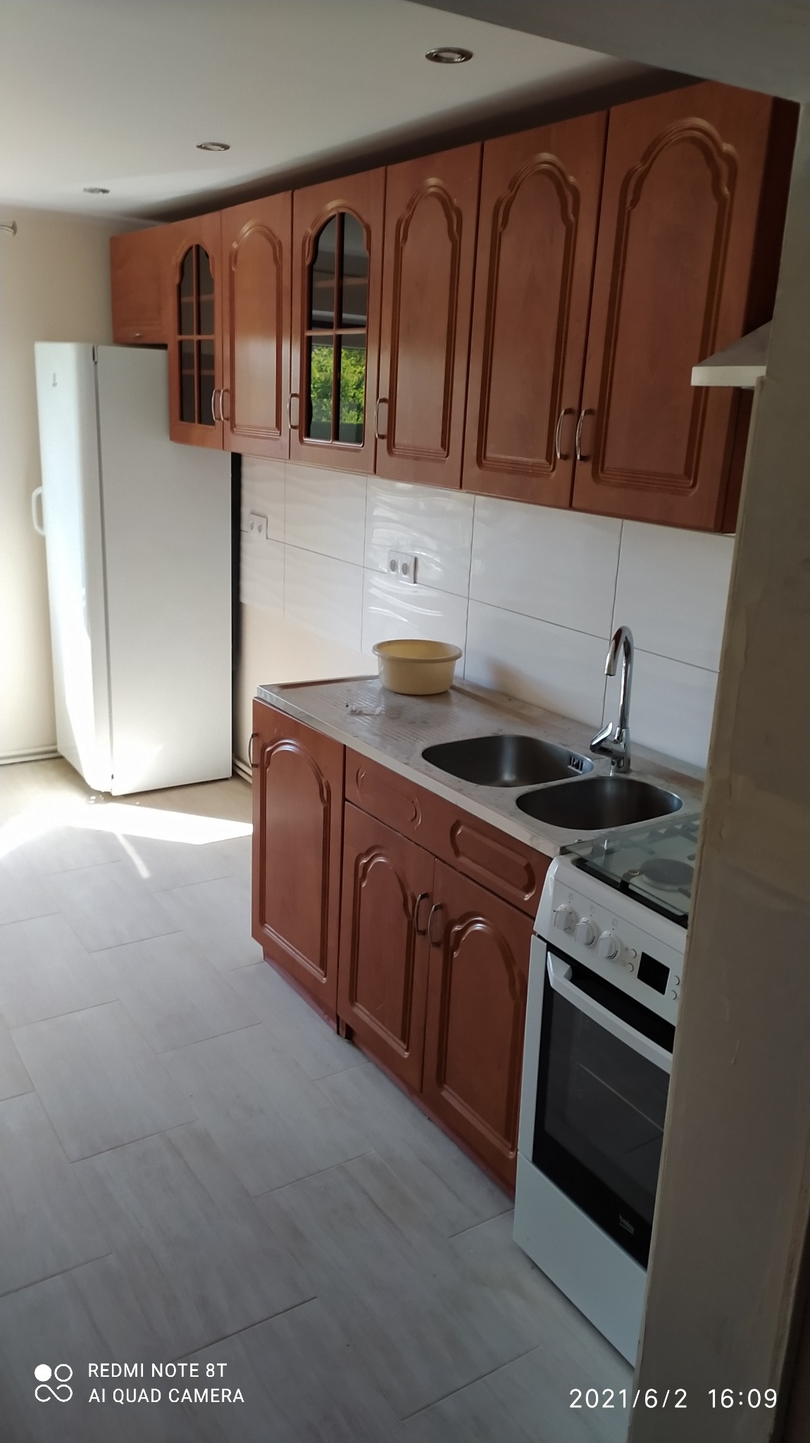 Wykończona kuchnia z brązowymi szafkami z zaokrąglonymi drzwiczkami, białymi płytkami na ścianie, dwukomorowym zlewem i białą lodówką.