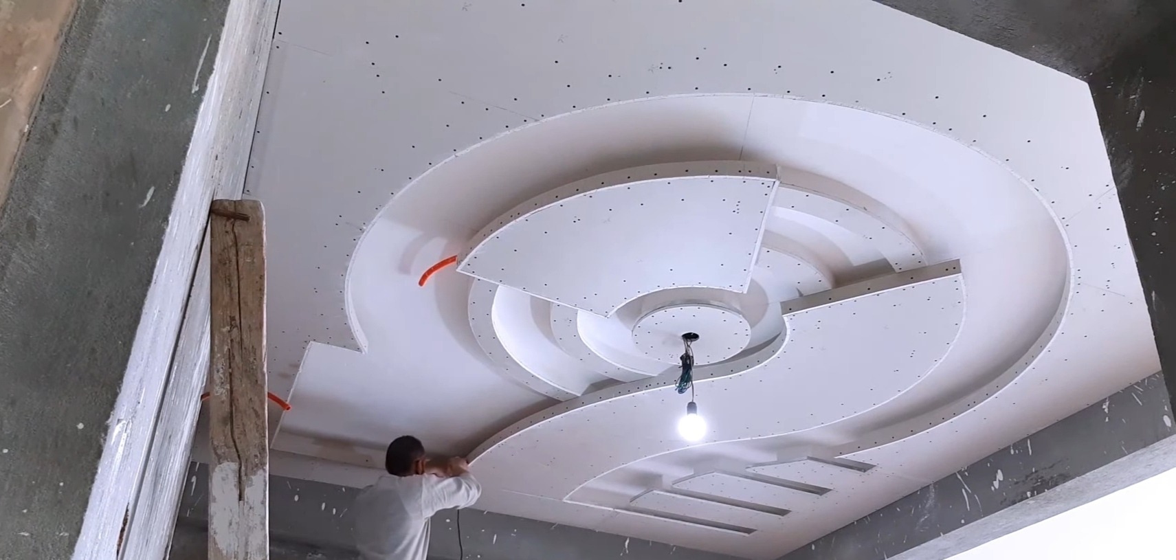 Pracownik montuje ozdobny sufit podwieszany z płyt kartonowo-gipsowych z okrągłymi elementami i miejscem na oświetlenie punktowe, widoczne wkręty mocujące.