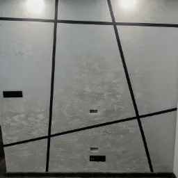 Ściana z dekoracyjną, szarą fakturą i czarnymi, ukośnymi liniami tworzącymi geometryczny wzór, uzupełniona o listwę przypodłogową i panele podłogowe imitujące drewno.