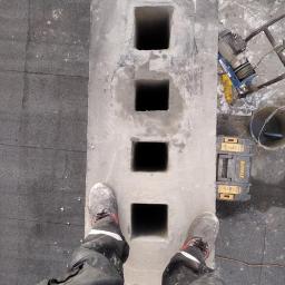 FachKOM Natalia Studzińska - Betonowy moduł kominowy z czterema otworami, widok z góry, obok skrzynka narzędziowa DeWalt, w tle wciągarka linowa, robocze buty na module.