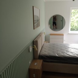 RADZIK Profesjonalne Usługi Elektryczno Budowlane Marek Radziwoniuk - Sypialnia po remoncie: pistacjowa ściana z lameli, łóżko z beżowym zagłówkiem, okrągłe lustro odbija fotografa. Nowoczesny design.