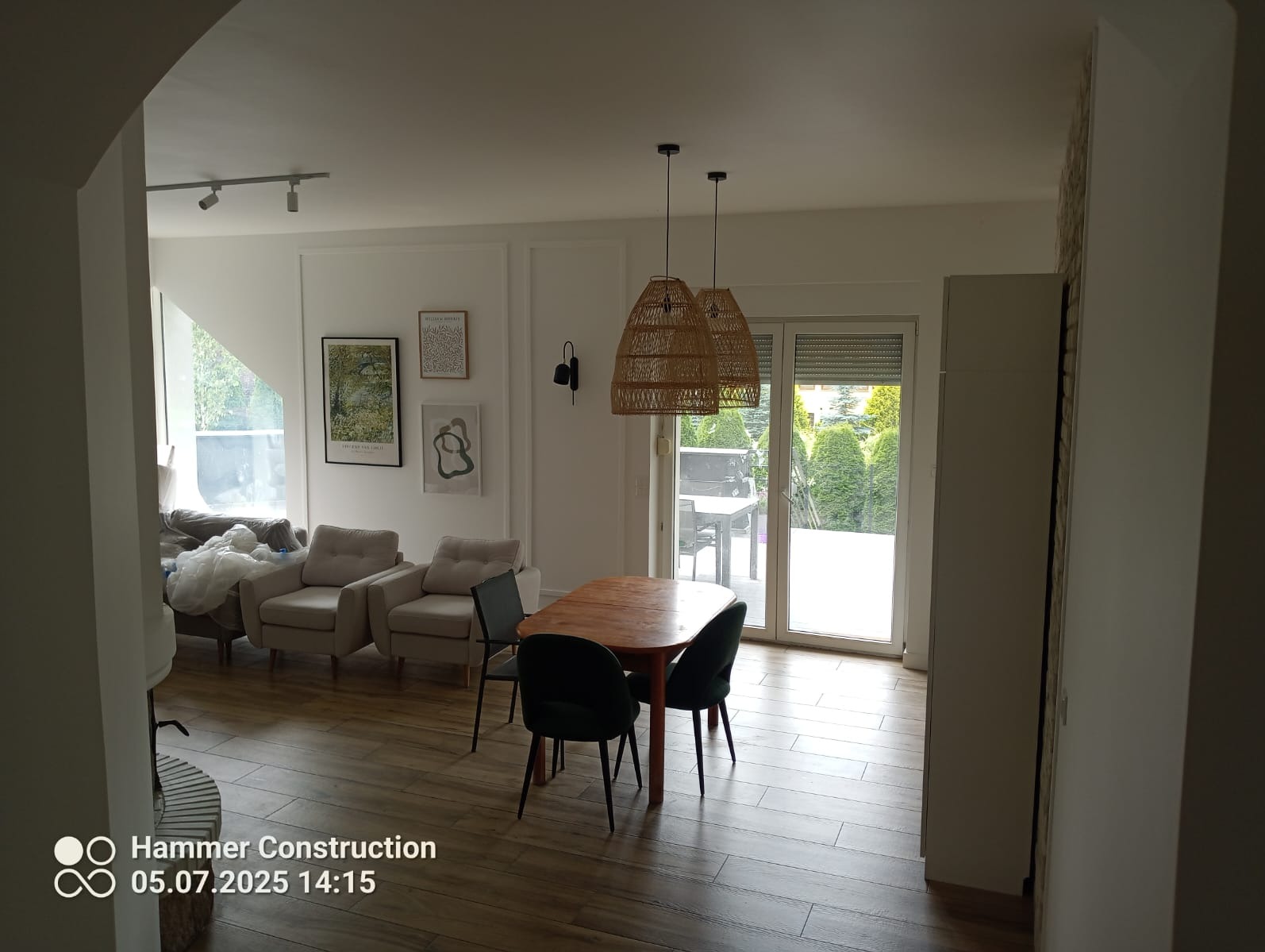 Jasne wnętrze po remoncie: drewniana podłoga, stół z krzesłami, widok na ogród przez przeszklone drzwi balkonowe, designerskie lampy i minimalistyczne dekoracje.