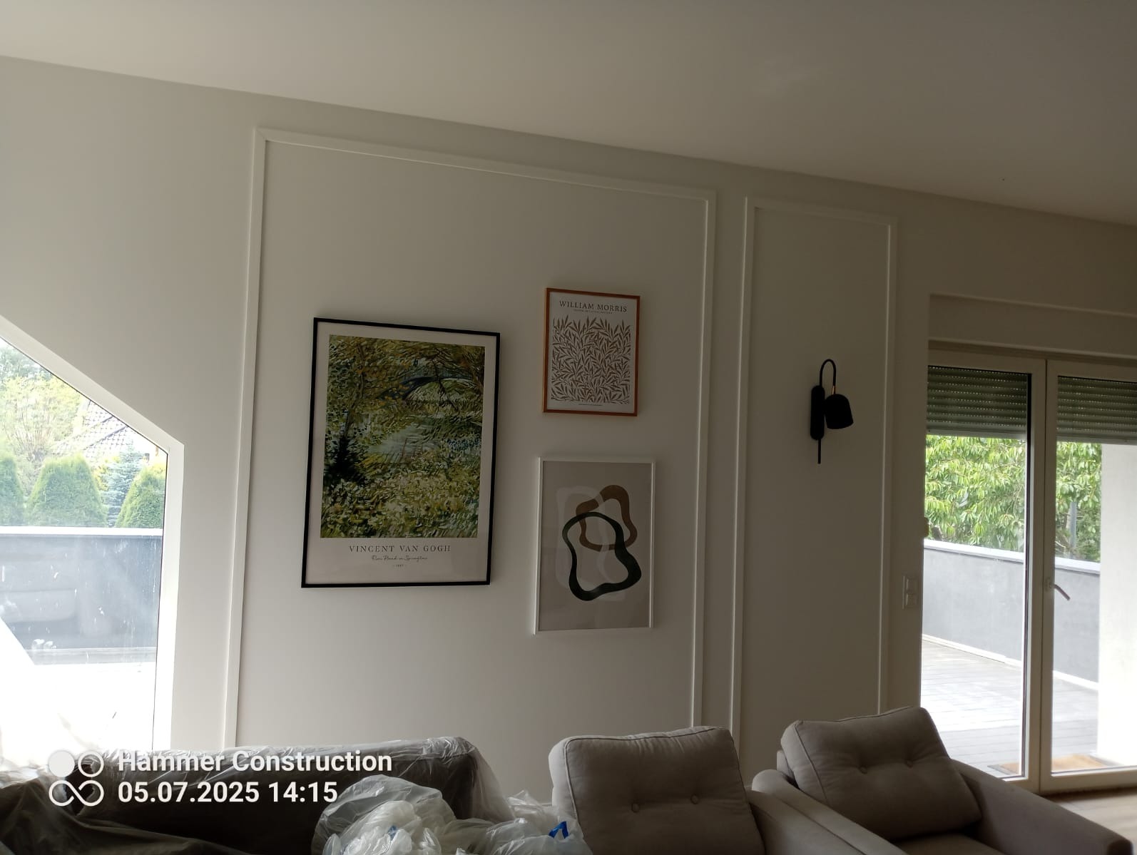 Białe ściany z dekoracyjnymi listwami i obrazami w salonie w Kartuzach. Widoczny fragment mebli pod folią ochronną.