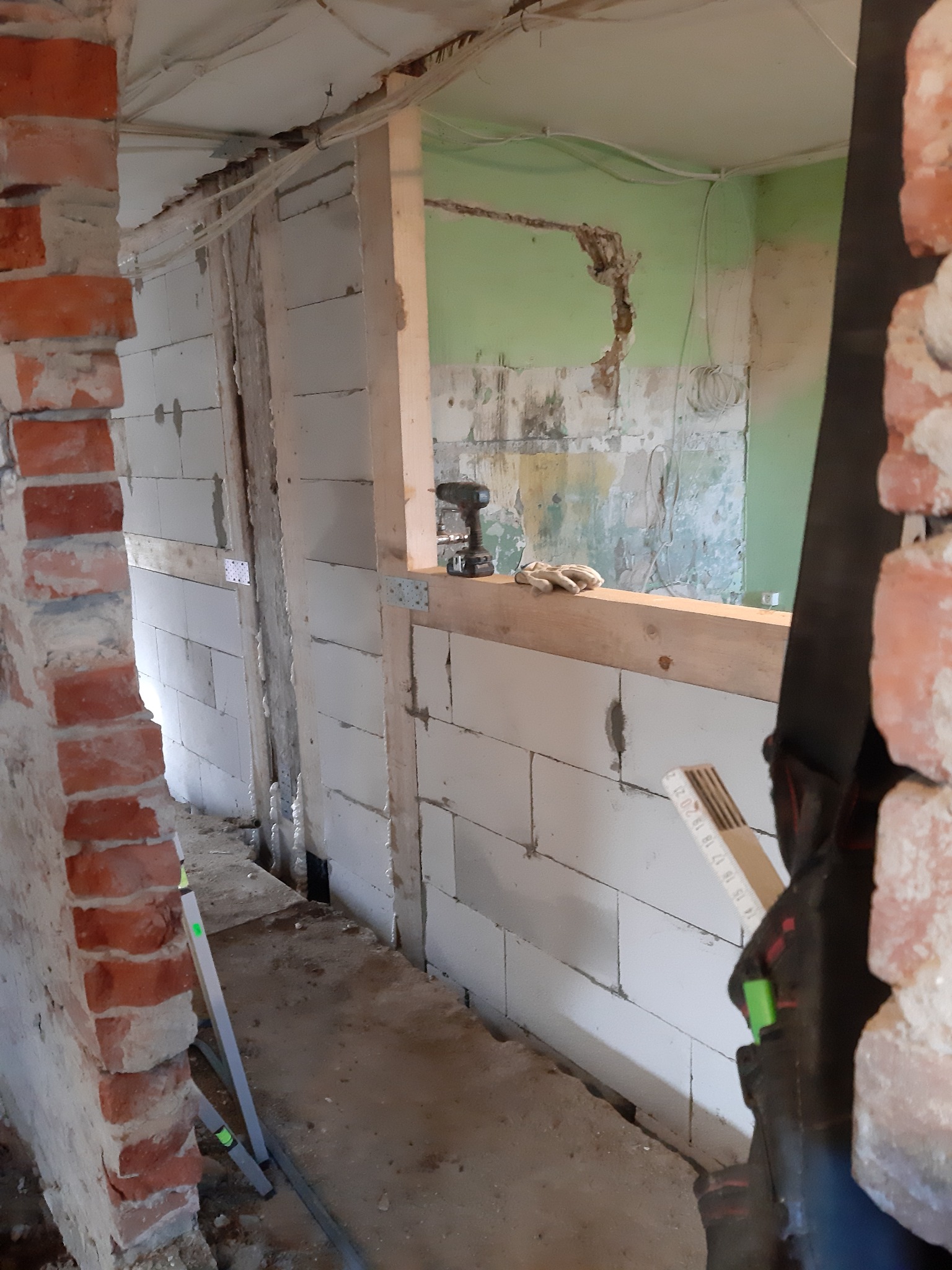 Wnętrze w trakcie prac murarskich z widocznymi bloczkami z betonu komórkowego, fragmentem ceglanej ściany, poziomnicą i narzędziami, przygotowywane do dalszych prac wykończeniowych.