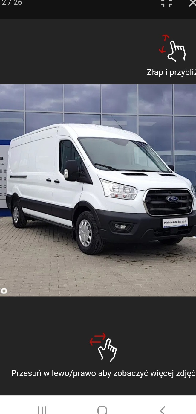 Biały samochód dostawczy Ford Transit na tle salonu samochodowego Plichta Auto Sp. z o.o. w Czaplinku, zaparkowany na kostce brukowej.