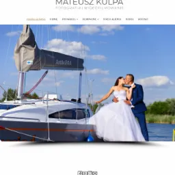 Para młoda w strojach ślubnych całuje się na pokładzie jachtu Antila 24.4, w tle woda i zieleń, zdjęcie zrealizowane przez firmę fotograficzną Mateusz Kulpa.