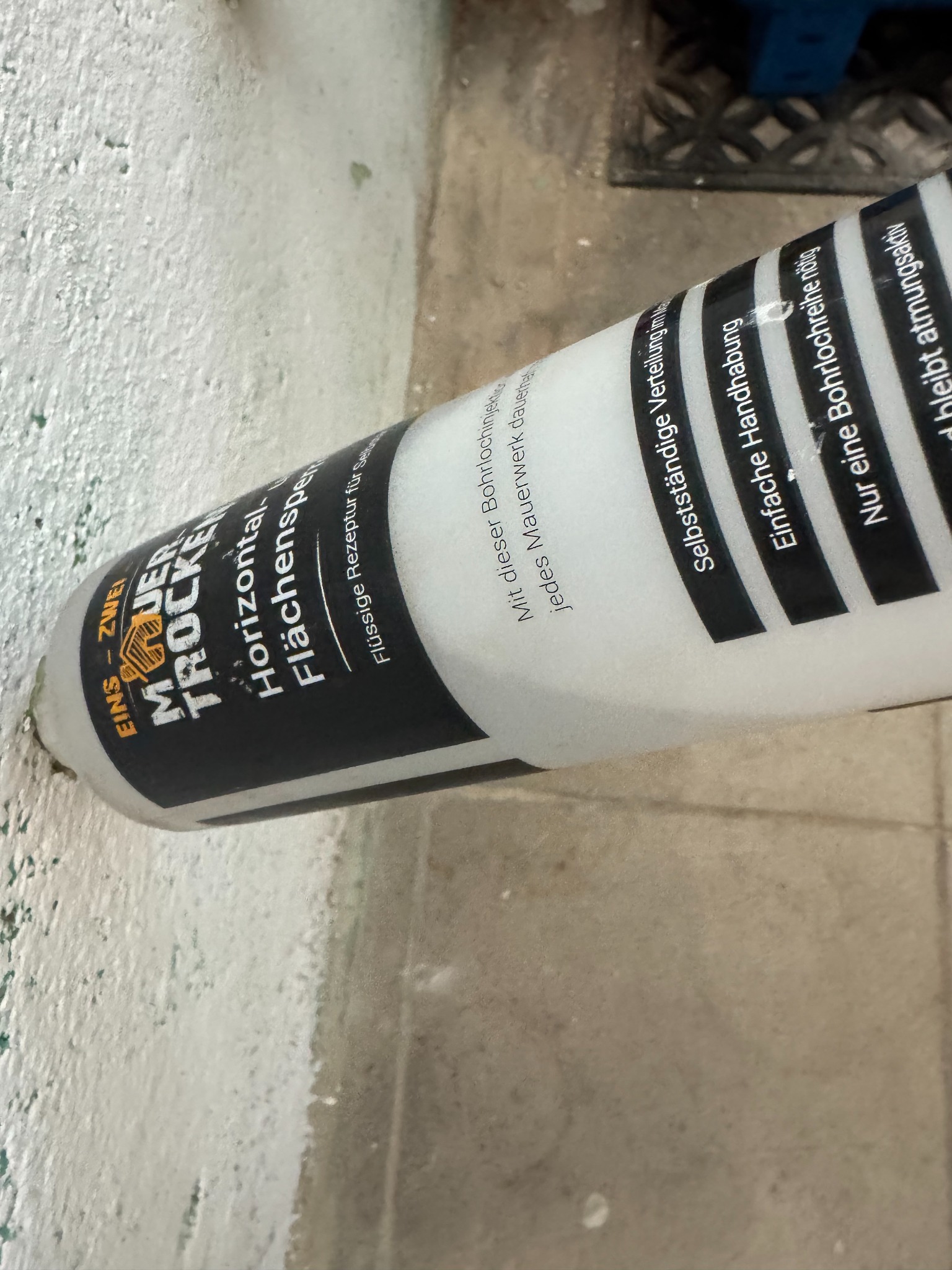 Preparat w białej butelce z czarnym napisem do iniekcji w mur. Produkt do samodzielnego stosowania, zapewniający trwałą ochronę przed wilgocią.