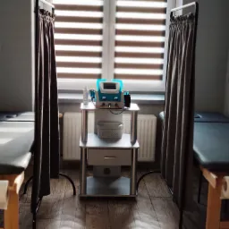 Gabinet z dwoma leżankami oddzielonymi zasłonami, centralnie ustawiony stolik z aparaturą do elektroterapii i ultrasonoterapii.