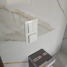 PM INSTALACJE Marcin Zimoch - Biały podwójny włącznik światła z gniazdkiem na marmurowej ścianie, obok kartonowe pudełko żarówki LED Lexman E27.