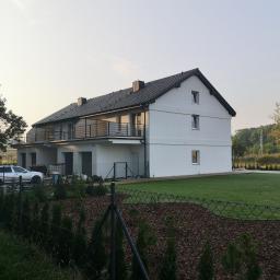 PM INSTALACJE Marcin Zimoch - Nowo wybudowany dwukondygnacyjny bliźniak z balkonami i czarną dachówką, ogrodzony siatką z widocznym samochodem i elementami wykończeniowymi na posesji.