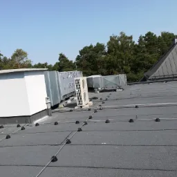 Instalacja odgromowa z przewodami i wspornikami na dachu budynku w Otwocku, widoczne jednostki klimatyzacyjne i wentylacyjne.