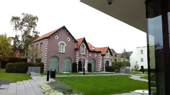 Odrestaurowany budynek z ceglanym dachem, pomalowany na różowo z białymi akcentami, otoczony zadbanym trawnikiem i elementami małej architektury, widoczna drabina oparta o fasadę.