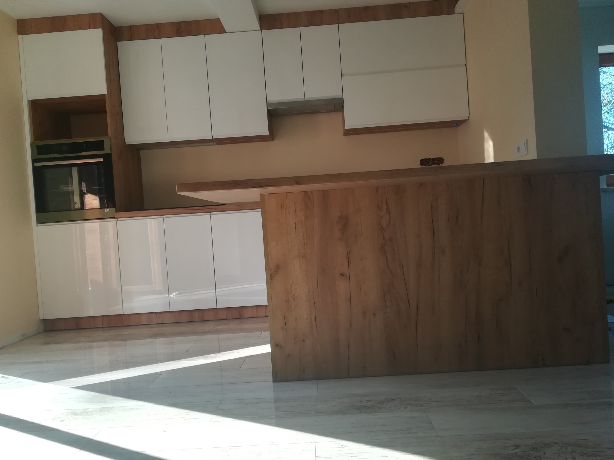 Nowoczesna, jasna kuchnia z białymi szafkami i drewnianym blatem w Jaworniku Polskim, z widoczną wyspą kuchenną z drewnianym fornirem i wbudowanym piekarnikiem.