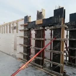 Budowa domu z bloczków betonu komórkowego: wznoszenie ścian z szalunkami i wspornikami, widoczne zbrojenia i elementy konstrukcyjne.
