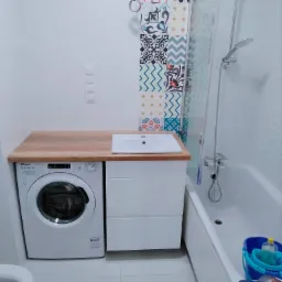 Łazienka w Strzelcach Wielkich z drewnianym blatem nad pralką i umywalką, kolorowe płytki dekoracyjne na ścianie, wanna z parawanem.