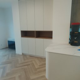 Dabek MNW - Biała zabudowa meblowa z otwartymi półkami w Hucina, widok na ułożoną w jodełkę podłogę i fragment blatu z narzędziami w tle.