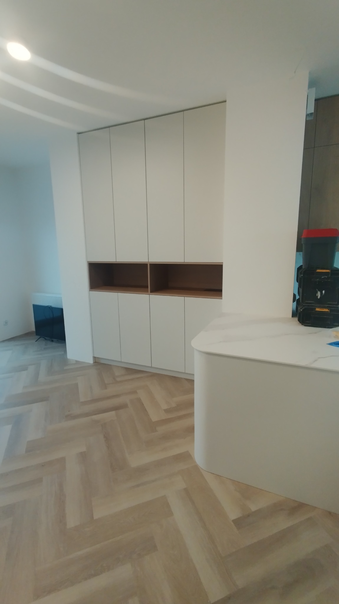 Biała zabudowa meblowa z otwartymi półkami w Hucina, widok na ułożoną w jodełkę podłogę i fragment blatu z narzędziami w tle.