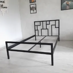 Czarna, metalowa rama łóżka z geometrycznym wezgłowiem, ustawiona w jasnym pokoju z dekoracjami ściennymi.