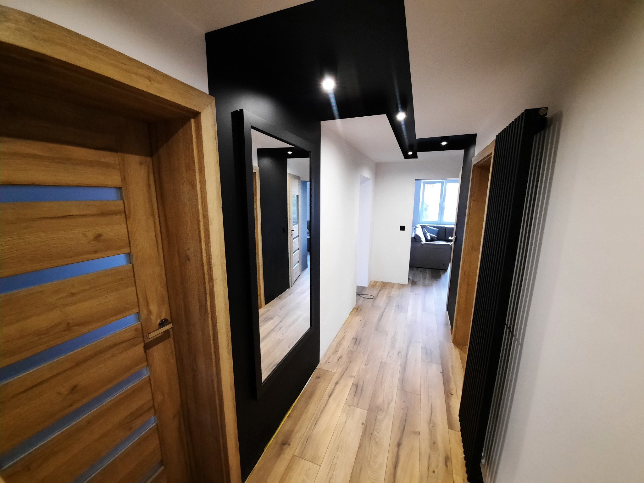 Nowoczesny przedpokój z drewnianą podłogą, drzwiami z przeszkleniami i czarnym sufitem podwieszanym z oświetleniem punktowym.