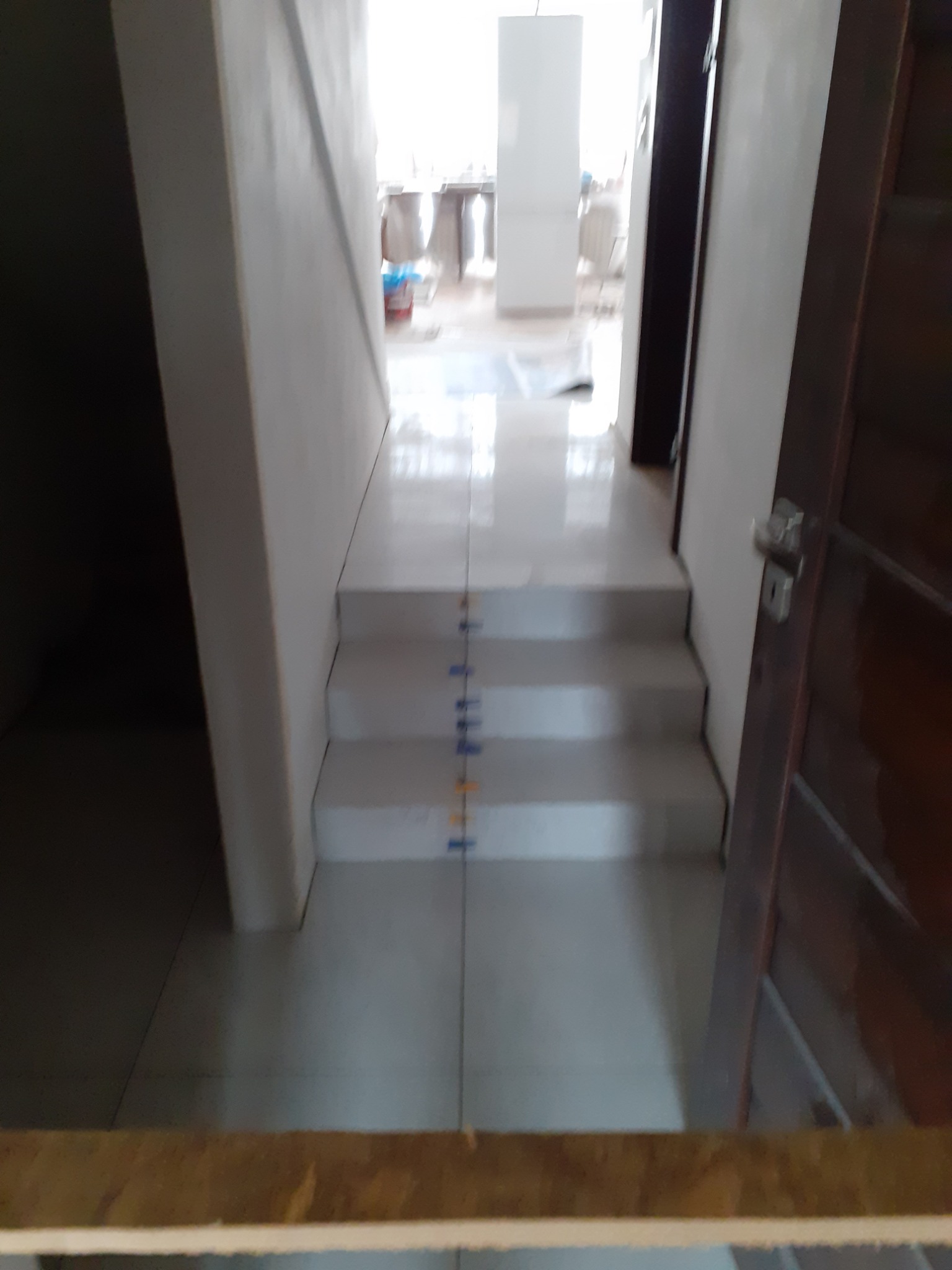 Wykończone schody z jasnymi płytkami, widoczne pionowe znaczniki fug, częściowo otwarte drzwi po prawej stronie.