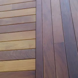 Fragment nowej, dwukolorowej podłogi z desek, z widocznymi śrubami mocującymi, ułożonej na zewnątrz budynku.