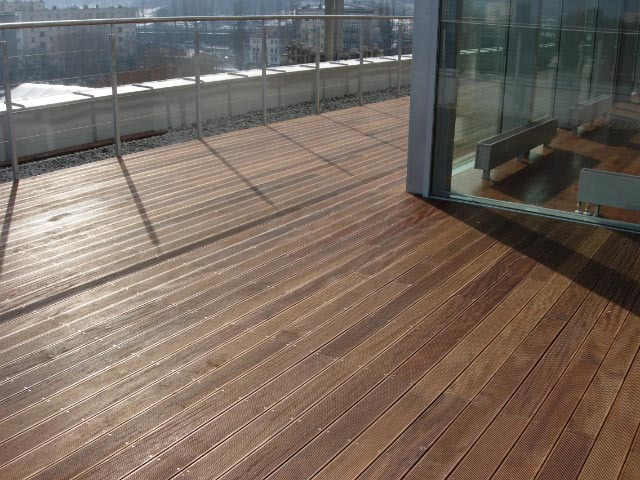 Wykończony taras z desek CUMARU w Instytucie Oceanografii w Gdyni, z widokiem na miasto w tle i metalową barierką.