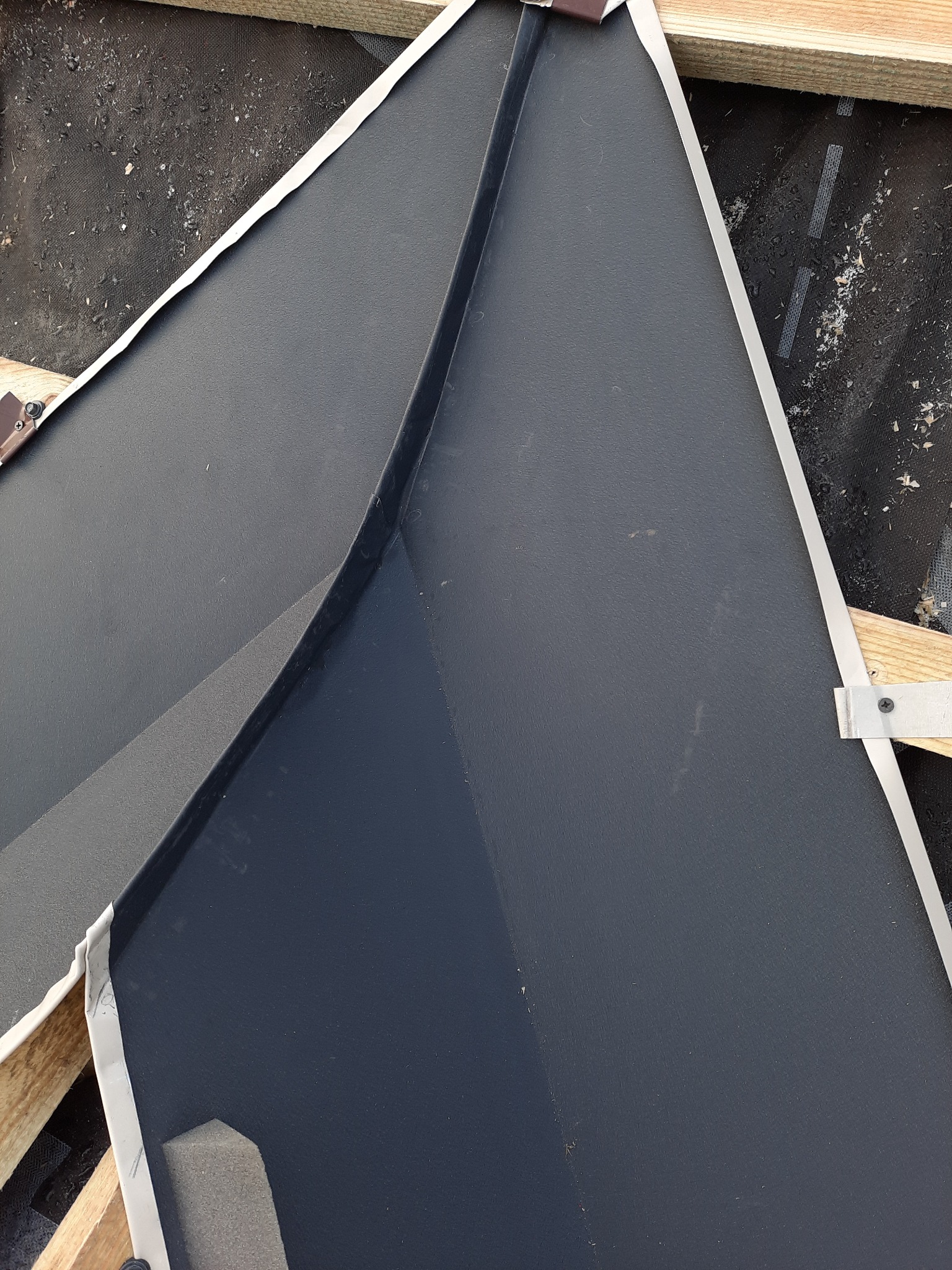 Fragment dachu pokrytego ciemną blachą trapezową z widocznymi drewnianymi łatami i membraną dachową, z bliska.