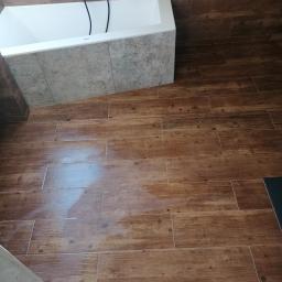 TechBud - Ukończona łazienka z wanną obudowaną szarą płytką i podłogą wyłożoną brązowymi płytkami imitującymi drewno, widok z góry.