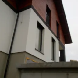 Nowoczesny dom jednorodzinny w Tarnowie z białą elewacją i drewnianym wykończeniem pod dachem, widoczny z perspektywy ogrodzenia.