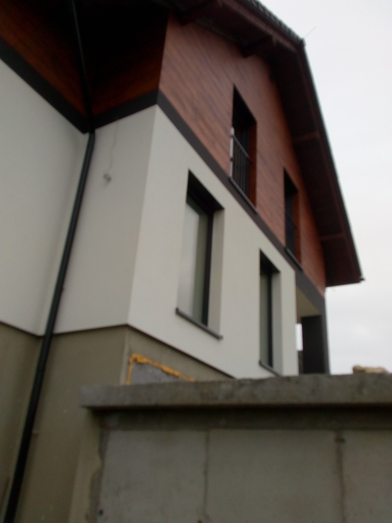 Nowoczesny dom jednorodzinny w Tarnowie z białą elewacją i drewnianym wykończeniem pod dachem, widoczny z perspektywy ogrodzenia.