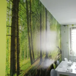 Fototapeta z motywem leśnym na ścianie jadalni; widoczny fragment ściany w kolorze limonkowym, st&oacute;ł z krzesłami w tle.