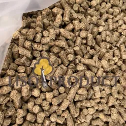 Zbliżenie na brązowe, cylindryczne pelety w przezroczystym worku, częściowo zasłonięte logo firmy.