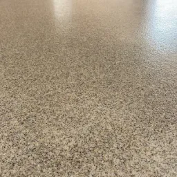 Jasna, błyszcząca posadzka z drobnym, wielobarwnym kruszywem, widoczna z niskiego kąta, ukazująca gładką powierzchnię z refleksami świetlnymi.