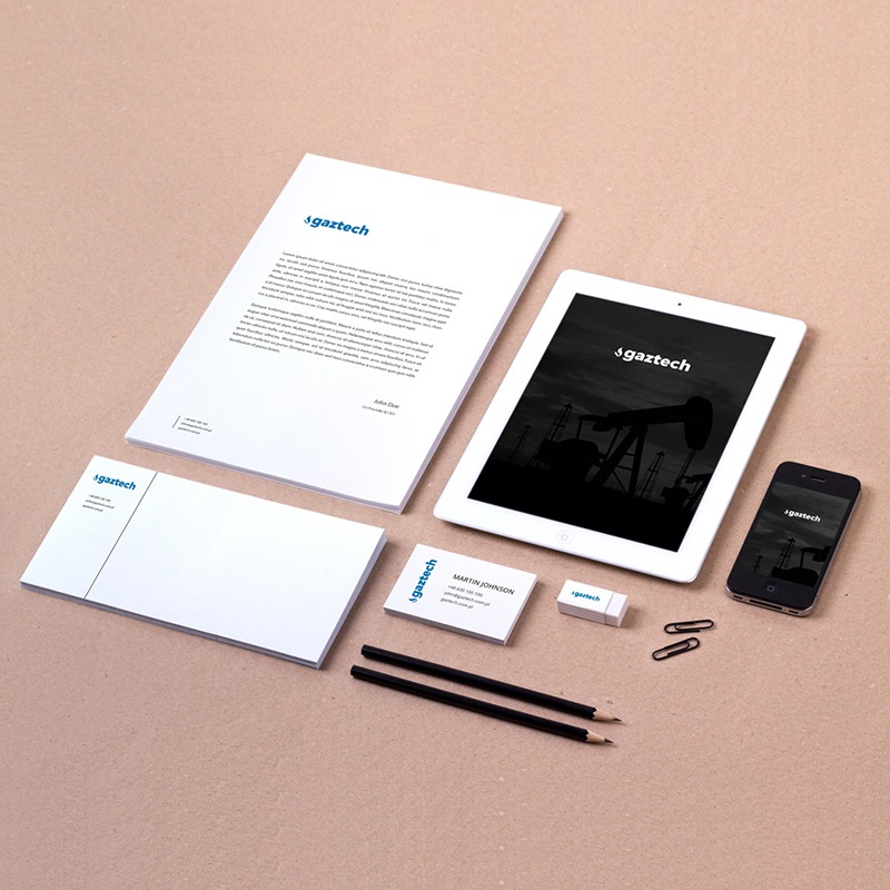 Komplet materiałów firmowych z logo 'gaztech' na papierze firmowym, wizytówce, notesie, pendrive, tablecie i smartfonie, ułożonych na beżowym tle.